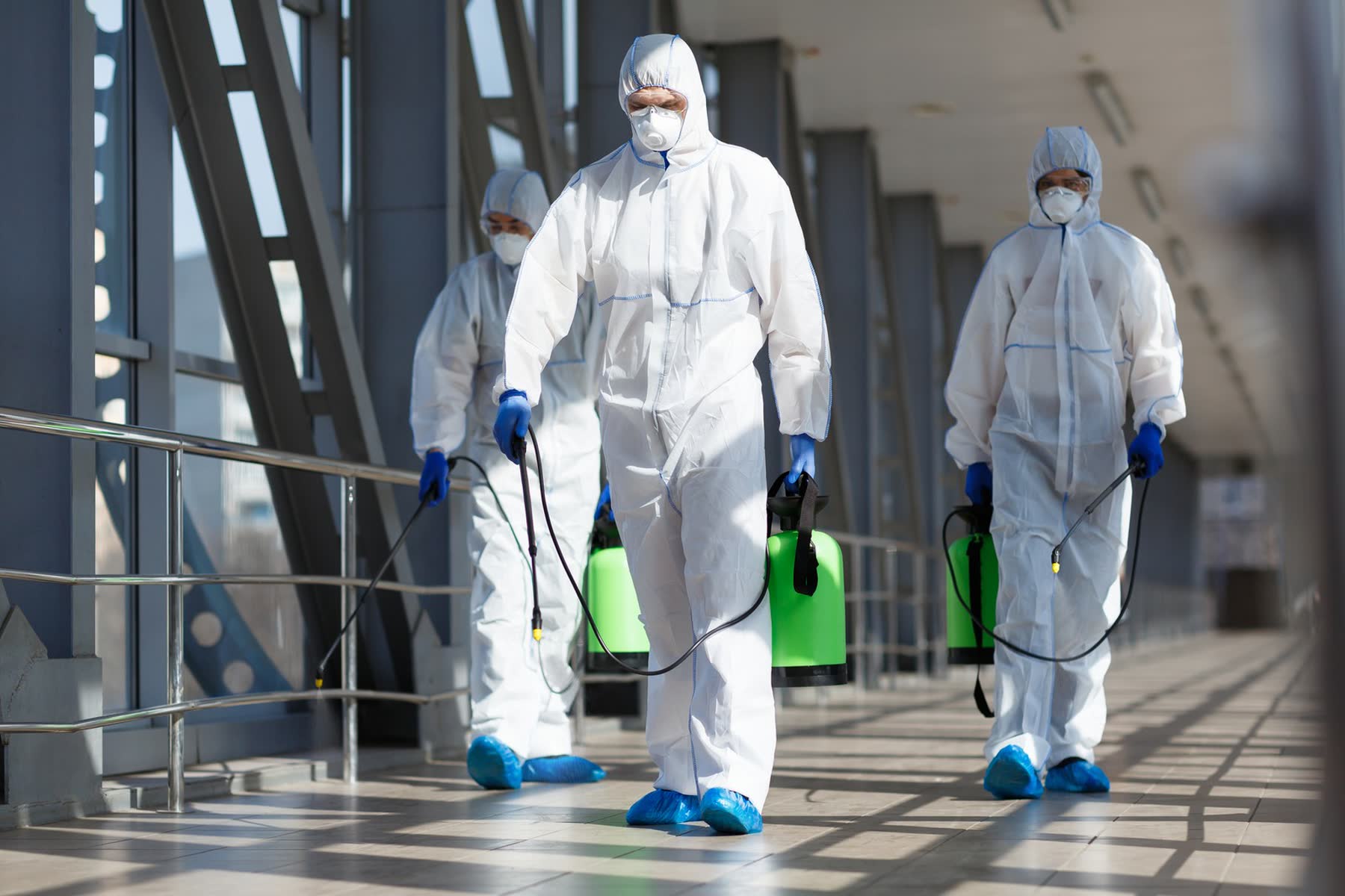 Hogan Cleaning Services technicians in protective suits carrying electrostatic sprayers through a commercial building